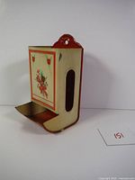 Side view of the antique tin litho match safe showing floral artwork and striker tray.