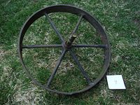 Front view of antique metal wheelbarrow wheel with six spokes and central axle, showing full circular shape on grass.
