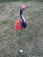 Front and side view of painted metal heron garden sculpture showing vibrant colors and metal tubing legs on grass.