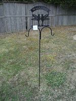 Full view of the 6 foot tall black metal shepherd's hook staked into grass, showing double hooks beneath the decorative welcome sign with hummingbirds.