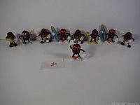 Photo showing all ten vintage California Raisins figurines lined up in a row on a white surface with a small paper marked '20'.