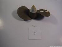 Photo showing two-blade propeller with olive-green paint, white shaft, and paper with number 8 for identification.