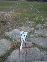 Front view of large metal bird sculpture with wireframe wings and painted spotted body outdoors on concrete