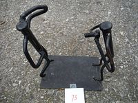 Front view showing two black painted metal rod figures on rectangular metal base.