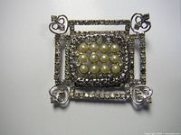 Front view of vintage brooch showing pearl center and rhinestone details on a silver-tone metal base.