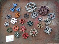 Full spread of 23 vintage valve handles arranged on a rusty metal surface showing various colors and shapes.