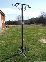 Full view of black metal birdhouse or plant stand with decorative hooks and sturdy base outdoors on grass