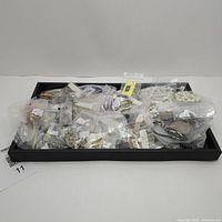 View of entire lot of costume jewelry, multiple small plastic bags with assorted jewelry inside on a black tray.