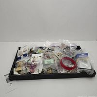Photo of assorted costume jewelry items in clear plastic bags and attached to display cards, spread on a black tray.