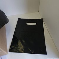 Folded black 9x12 inch plastic retail bag with die-cut handle showing size and material.