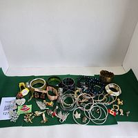 Overview of assortment of costume jewelry laid on green cloth including bracelets, brooches, pins, and earrings.