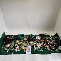 Wide view of assorted costume jewelry on green cloth showcasing a variety of bracelets, necklaces, pendants, earrings, and brooches spread out neatly.