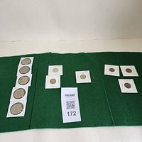 Overview of all coins spread on green felt showing Canadian and French coins in individual holders.