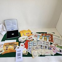Wide layout showing assortment of mixed stamps mostly Canadian themes and a Canadian coin set in a box on green felt background.