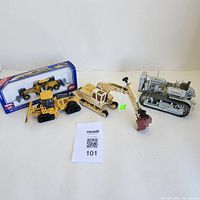 Main photo showing all four die-cast metal vehicles including vintage digger, yellow bulldozer, gray crawler tractor, and boxed motorgrader toy