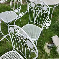Four white metal patio chairs with floral decorative backs and mesh seats on grass