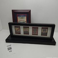 Two framed vintage matchbook collections displayed on a white surface. One frame reddish wood with Army Air Force Pilot School design, other black frame with four vintage auto oil matchbooks.