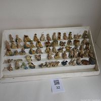 Wide view of 60 assorted Wade ceramic figurines displayed on a white tiered tray, showing full set in used condition with various designs.