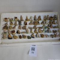 Wide view of 60 assorted Wade figurines arranged on white stepped display holding small ceramic animals, characters, and cottages.