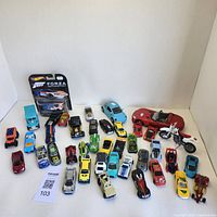 Wide view of all die cast cars and white dirt bike arranged on white surface.