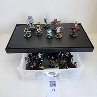 Mage Knight miniature figures displayed on a black tray and a plastic container below with several more figures packed inside.