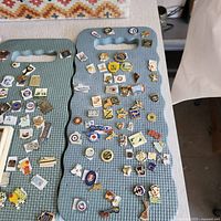 Three foam pin boards with numerous vintage assorted enamel and metal collectible pins of various styles and themes across several decades.