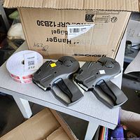 Two Monarch 1136 double line pricing guns on a table next to a roll of white pricing tags.