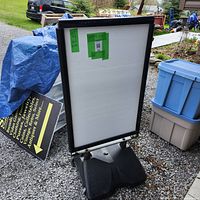 Overall front view of retail sidewalk sign with white display panel and black frame on sand-filled base.