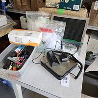 Overall view of lot showing shipping scale, tagging gun, loop pins, and bin of pens on white table.