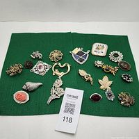 Lot of 18 vintage brooches with varied designs laid out on green mat, showing overall assortment