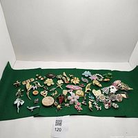 Wide view of entire lot of vintage brooches and pins spread on green cloth