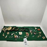 Wide view of entire jewelry lot arranged on green felt including bracelets, pins, brooches, and earrings