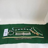 Full view of the six vintage jewelry pieces arranged on green felt including five bracelets and one necklace.