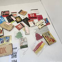 Full overhead view of assortment of vintage matchbooks, matchboxes, ashtrays and cigarette holder accessories on white background.