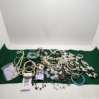 Overview of assorted costume jewelry including pearl necklaces, bracelets, earrings, and pendants displayed on green fabric.