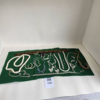 Full view of the jewelry lot laid out on a green cloth showing various necklaces, bracelets, and earrings.