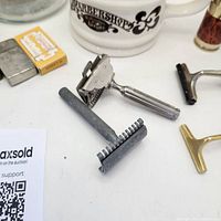 Close-up of two metal safety razors and razor blades pack with ceramic shaving mug in background