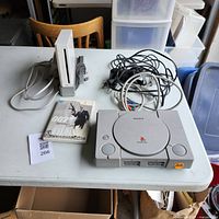 Nintendo Wii console, Sony PlayStation console, one controller, cables, and 007 game case displayed on a table
