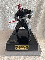 Darth Maul action figure holding double-bladed red lightsaber standing on black base with Star Wars logo, facing slightly to the right.