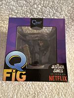 Front angled view of the Jessica Jones Q-Fig collectible in purple box with window, showing figure partially visible inside.