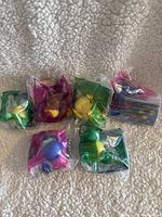 Overall view of the 6 Pokemon Happy Meal toys in original sealed plastic packaging with colorful backing cards, laid out on a beige textured surface.