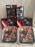Two Star Wars themed metal lunch boxes, two matching metal plates, a metal money box with Stormtrooper design, and a boxed 50-piece Star Wars The Force Awakens puzzle arranged on a textured light background.