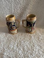 Two vintage West Germany beer steins showing front and side views of their detailed colorful raised relief scenes and German inscriptions.