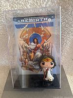 Wonder Woman Funko Pop figurine displayed inside a clear acrylic case with a backdrop insert of Wonder Woman Rebirth #6 comic cover art.