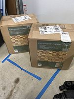 Photo showing two unopened boxes of Acacia wooden flooring tiles with labels and shipping stickers.