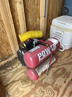 Side view of the red Power System Plus air compressor tank showing the brand name and attached yellow hose.