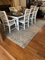 Area rug under dining table with white chairs on hardwood floor, shows color and size with furniture setup.