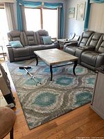 Living room with the area rug placed under a coffee table, surrounded by recliner sofas, showing color and size of the rug in the space.