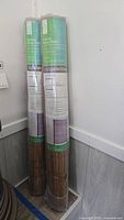 Two rolled bamboo shades standing upright in clear plastic packaging, with green and white labels.