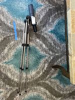 Folded tripod and spotting scope on carpet, showing attached price label.